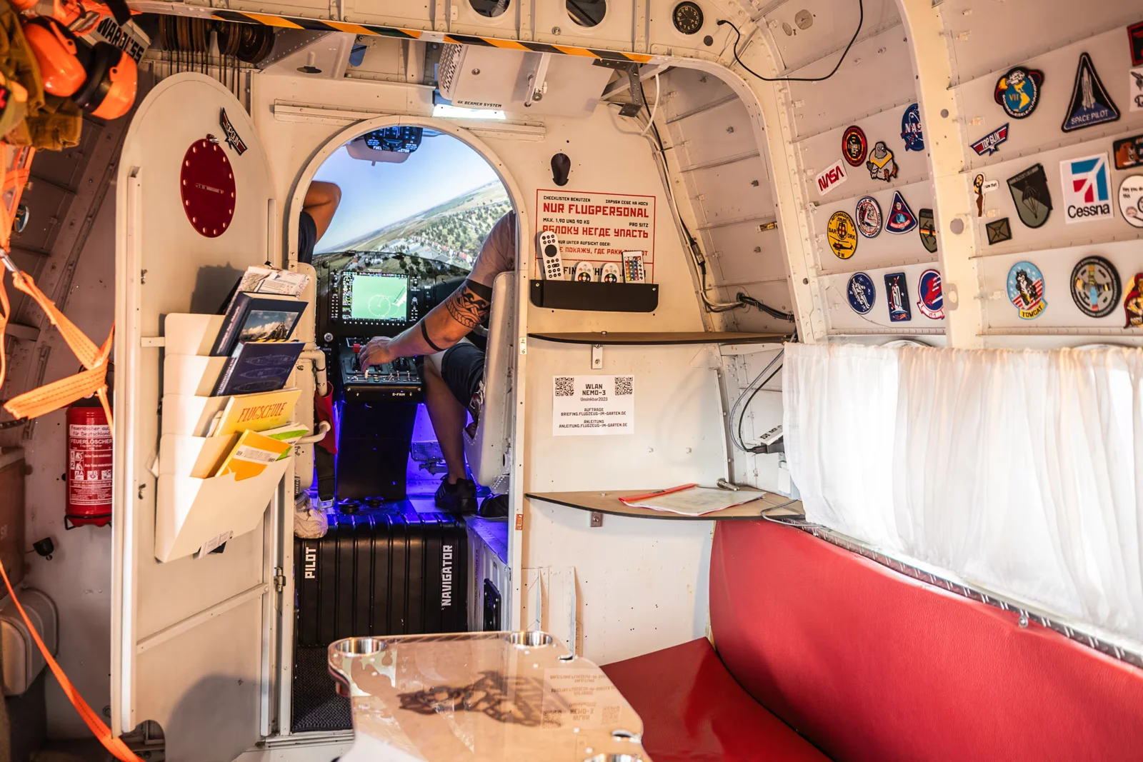 Blick durch die Antonov-Kabine mit roter Sitzbank, Tisch und geöffnetem Cockpit